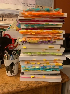 A stack of over 20 books with many small post-it’s on their pages
